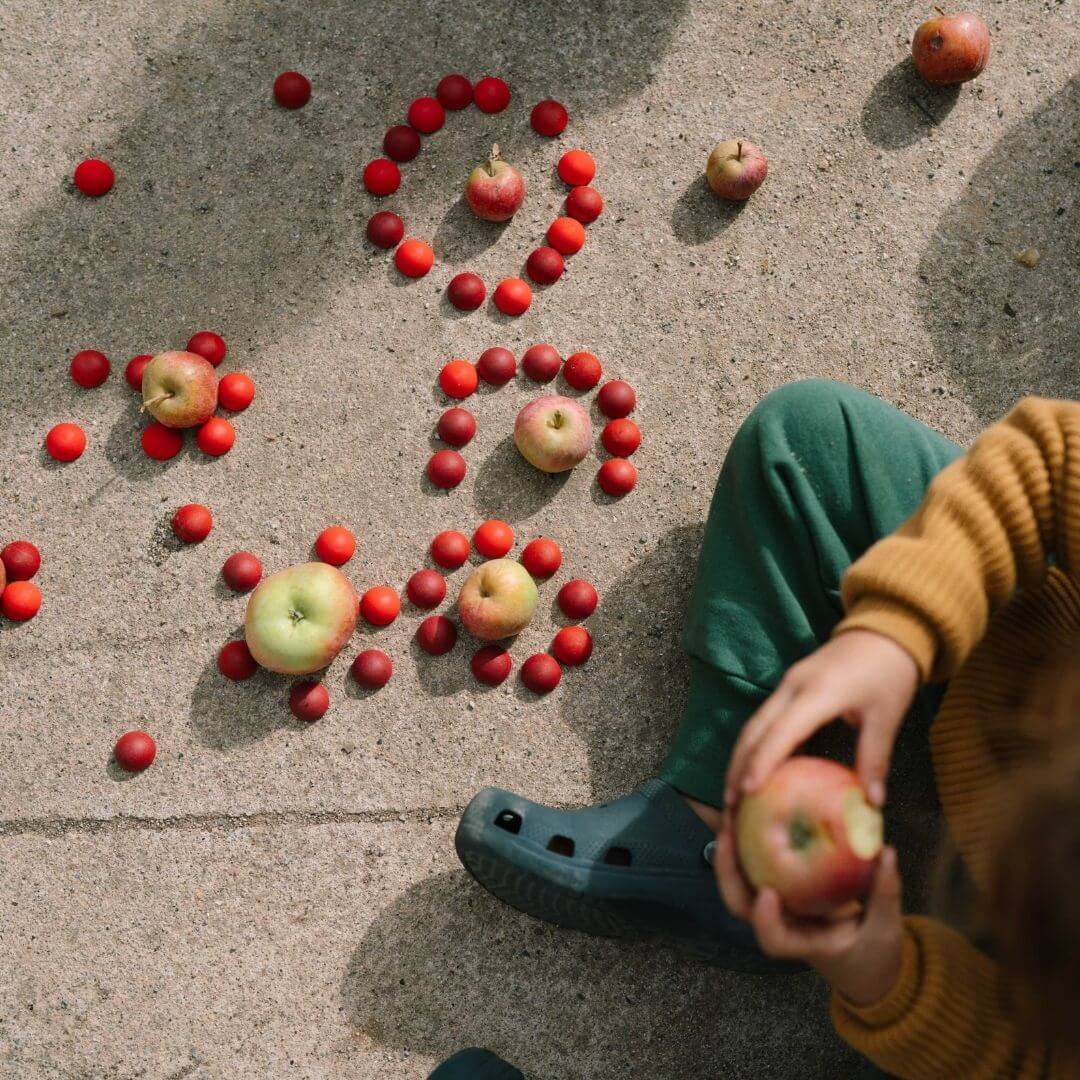 Grapat Mandala Half Spheres set with 36 small red hand-painted wooden half spheres arranged in a circular pattern outside on pavement with apples and a child nearby - Bella Luna Toys