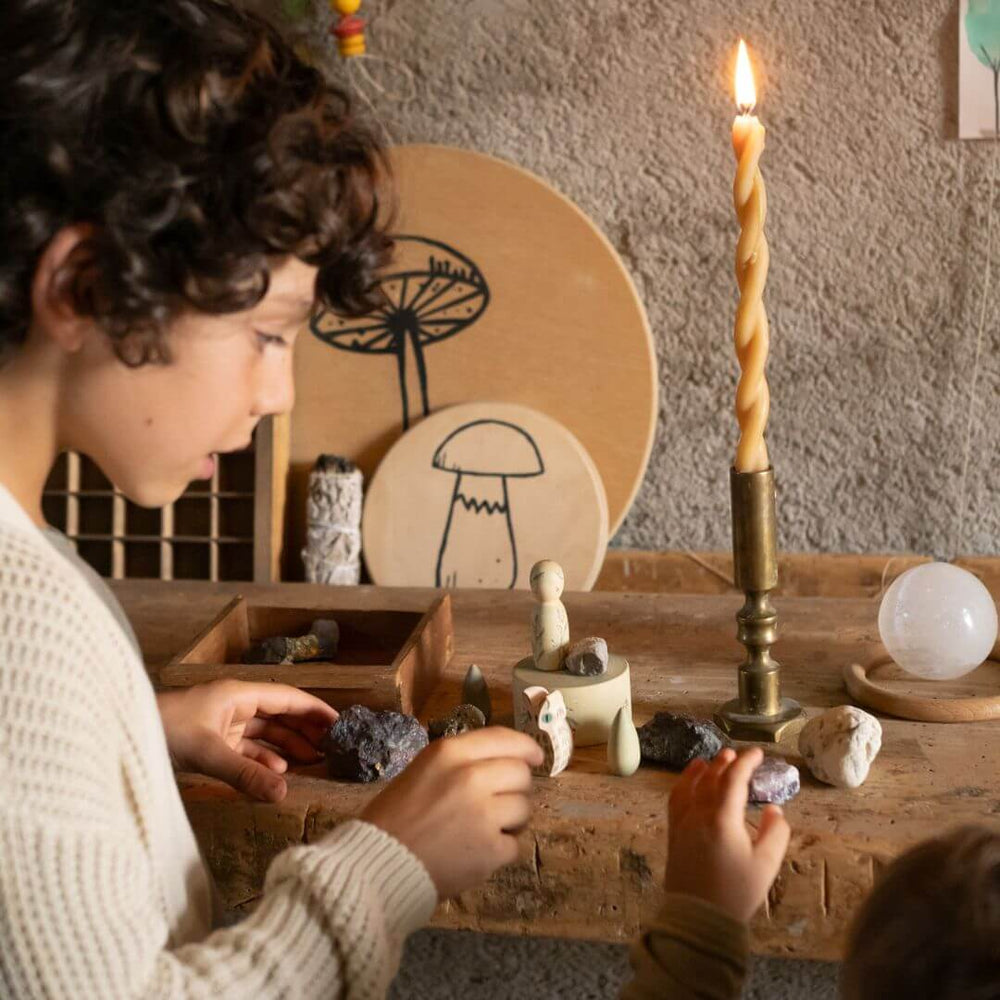 Child interacting with small figurines and crystals on a wooden table with a candle in the background. Grapat Hello Winter set