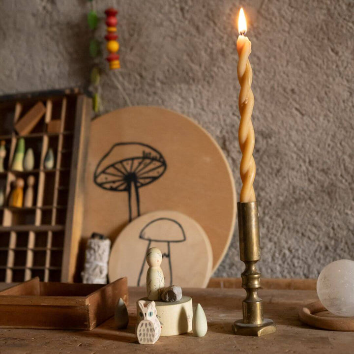Candle in a brass holder on a wooden surface with decorative items and a textured wall background. Grapat Hello Winter set