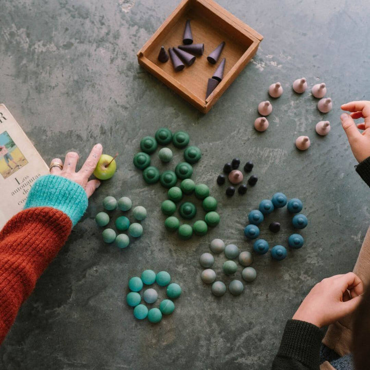 Children playing with and arranging the Grapat Mandala Mix Cold set with 81 hand-painted wooden mandala pieces in blue, green, and purple tones on a concrete surface - Bella Luna ToysBella Luna Toys