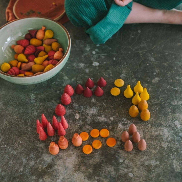 Grapat Mandala Mix Warm set with 81 hand-painted wooden mandala pieces in red, orange, and yellow tones shown in play with a child nearby - Bella Luna Toys