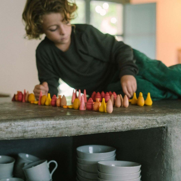 Grapat Mandala Mix Warm set with 81 hand-painted wooden mandala pieces in red, orange, and yellow tones shown on a counter with a child playing - Bella Luna Toys