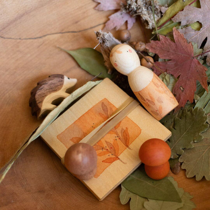 Grapat x Ostheimer Hello Autumn! wooden play set with figure, hedgehog, mushrooms, and illustrated box displayed among colorful autumn leaves – Bella Luna Toys.