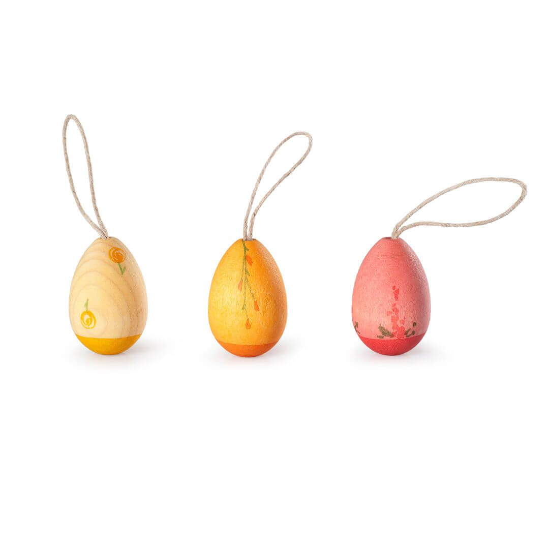 A set of three handcrafted wooden Easter egg ornaments from Grapat, arranged in a row against a white background. Each egg features warm, sunrise-inspired colors in shades of yellow, orange, and red, with a natural wood texture and delicate painted details. Each ornament has a looped string for hanging, making them perfect for festive Easter decorations.
