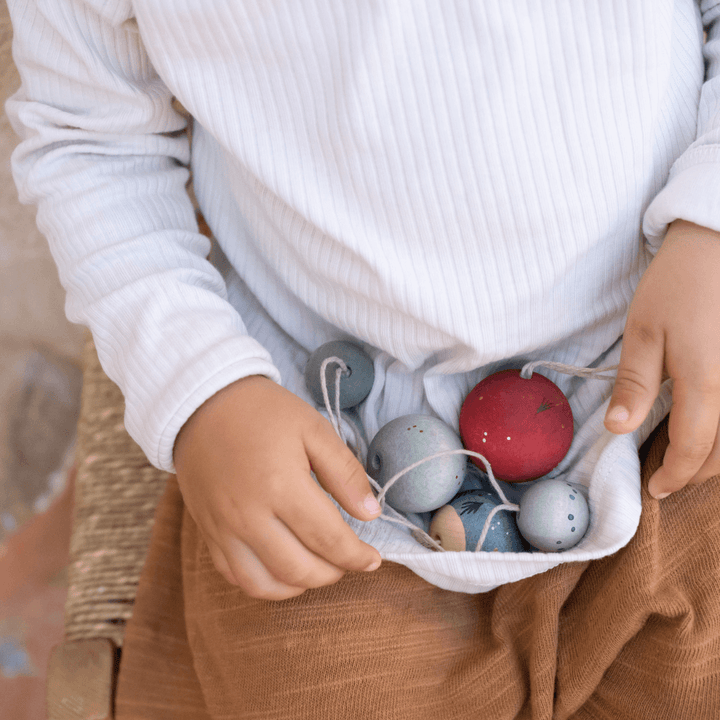 Child holding several Grapat Wish Balls Wooden Ornaments with hanging threads in the fold of a white shirt – Bella Luna Toys.