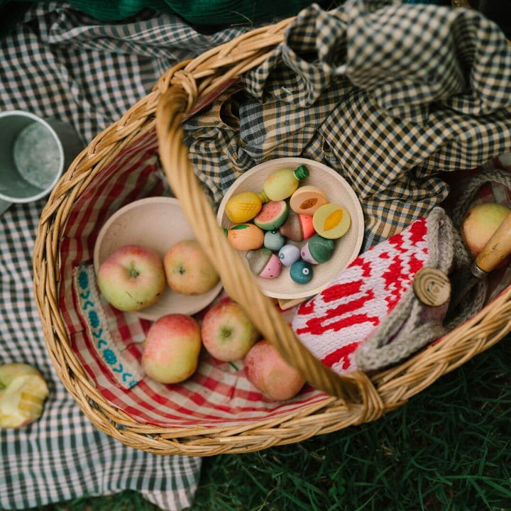 Grapat wooden fruits set with 12 hand-painted wooden fruit pieces in assorted shapes and soft natural colors displayed in a picnic basket and picnic setting - Bella Luna Toys