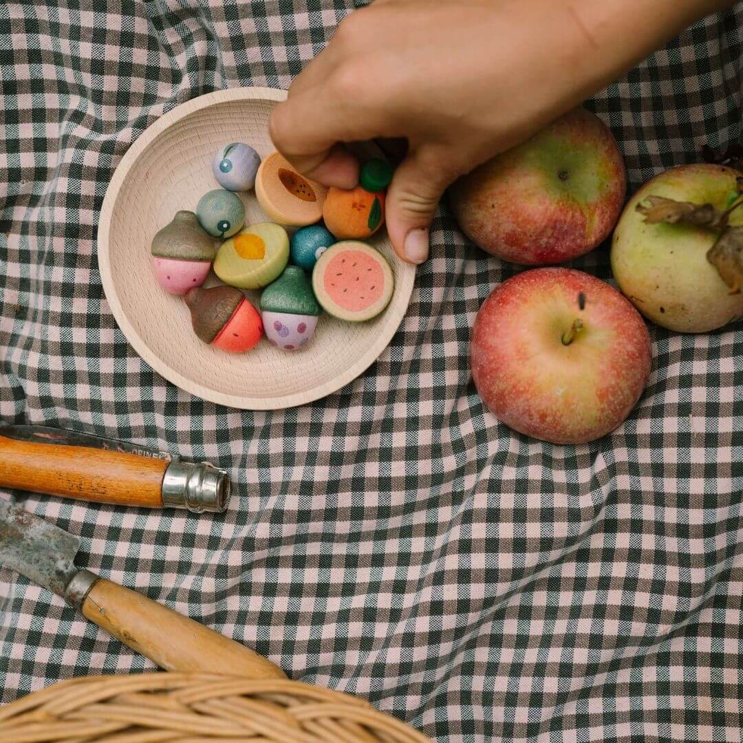 Grapat wooden fruits set with 12 hand-painted wooden fruit pieces in assorted shapes and soft natural colors displayed on a black and white gingham tablecloth with apples - Bella Luna Toys