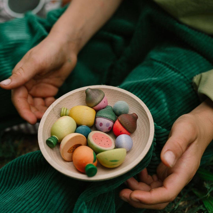 Grapat wooden fruits set with 12 hand-painted wooden fruit pieces in assorted shapes and soft natural colors displayed in a wooden dish set on a child's knee - Bella Luna Toys