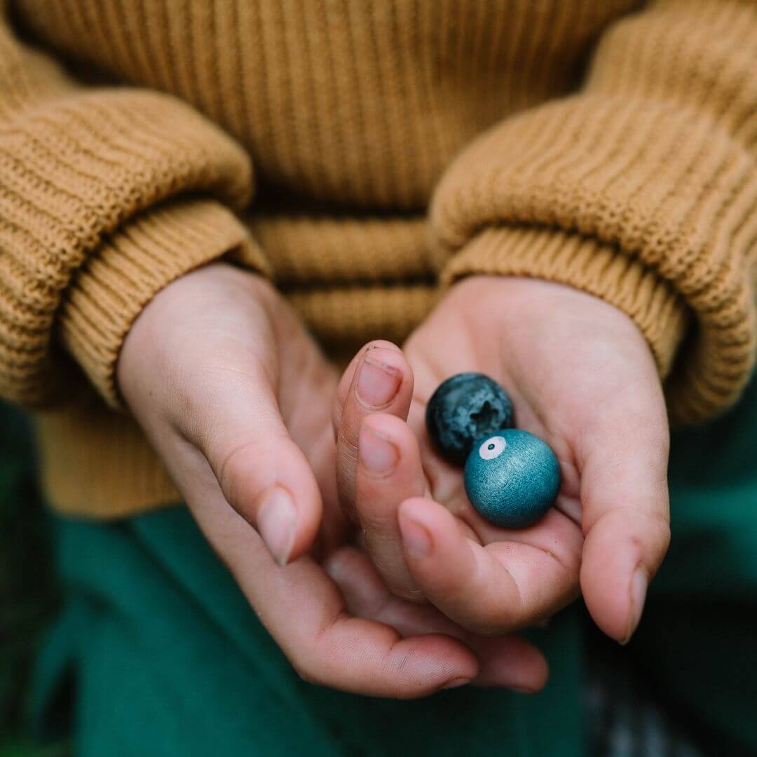 A child's hand holding 2 Grapat wooden blueberries - Bella Luna Toys 