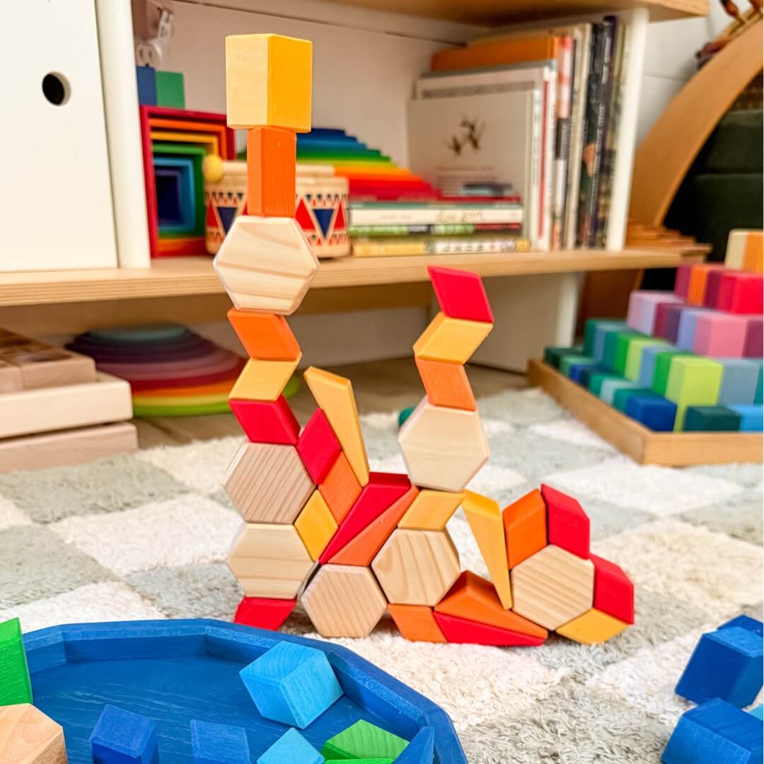Colorful wooden building blocks on a carpeted floor with a bookshelf in the background