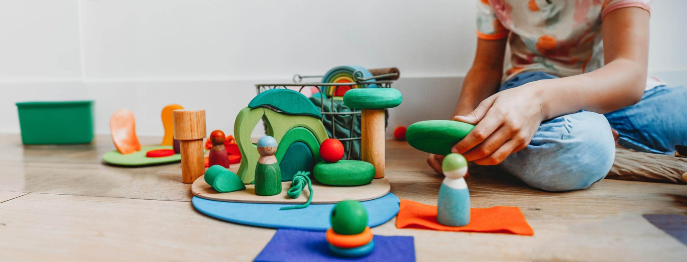 Child playing on wooden floor with green Grimm's wooden toys and peg figures