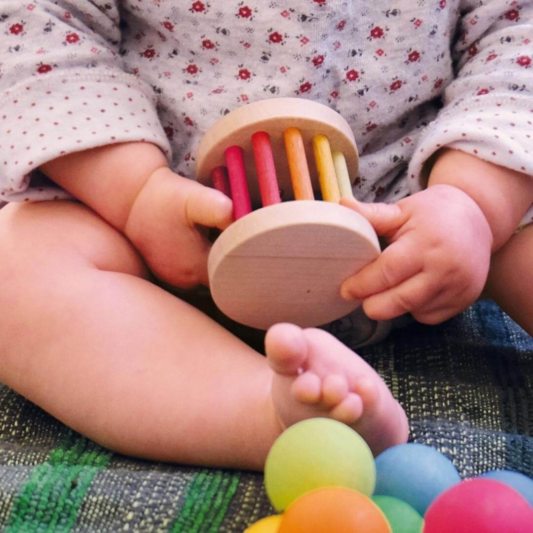 A baby holding the Grimm's Spiel & Holz - Grimm's Mini Rolling Wheel - Bella Luna Toys