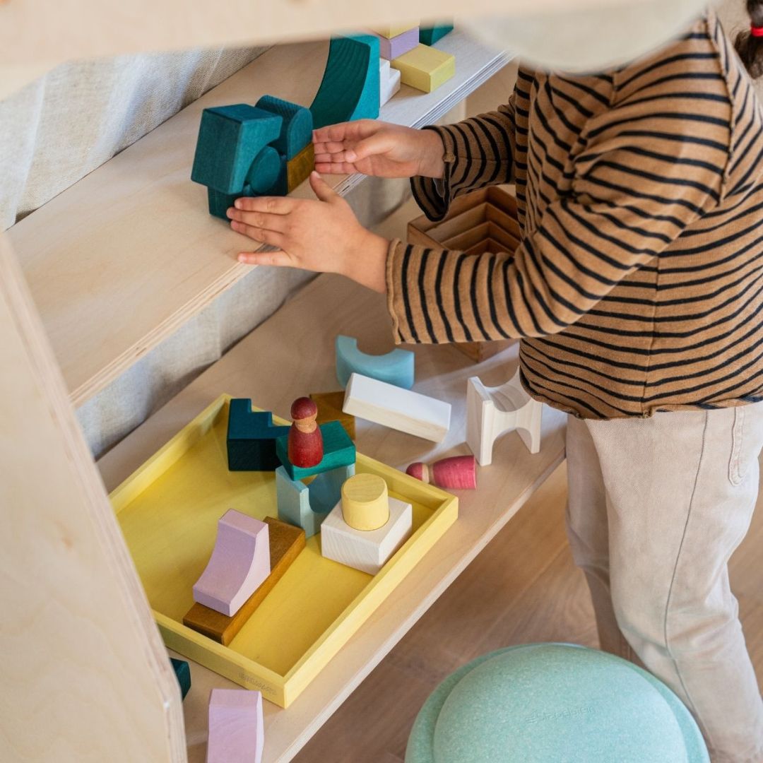 A child building with blocks from the Grimm's Wooden Toys Tiny Art Collection.