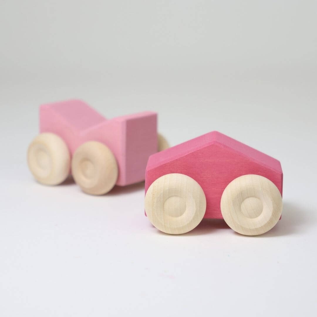Two pinkwooden stacking cars by Grimm’s, handcrafted with natural wood wheels and smooth, colorful bodies—perfect for open-ended building and rolling play.