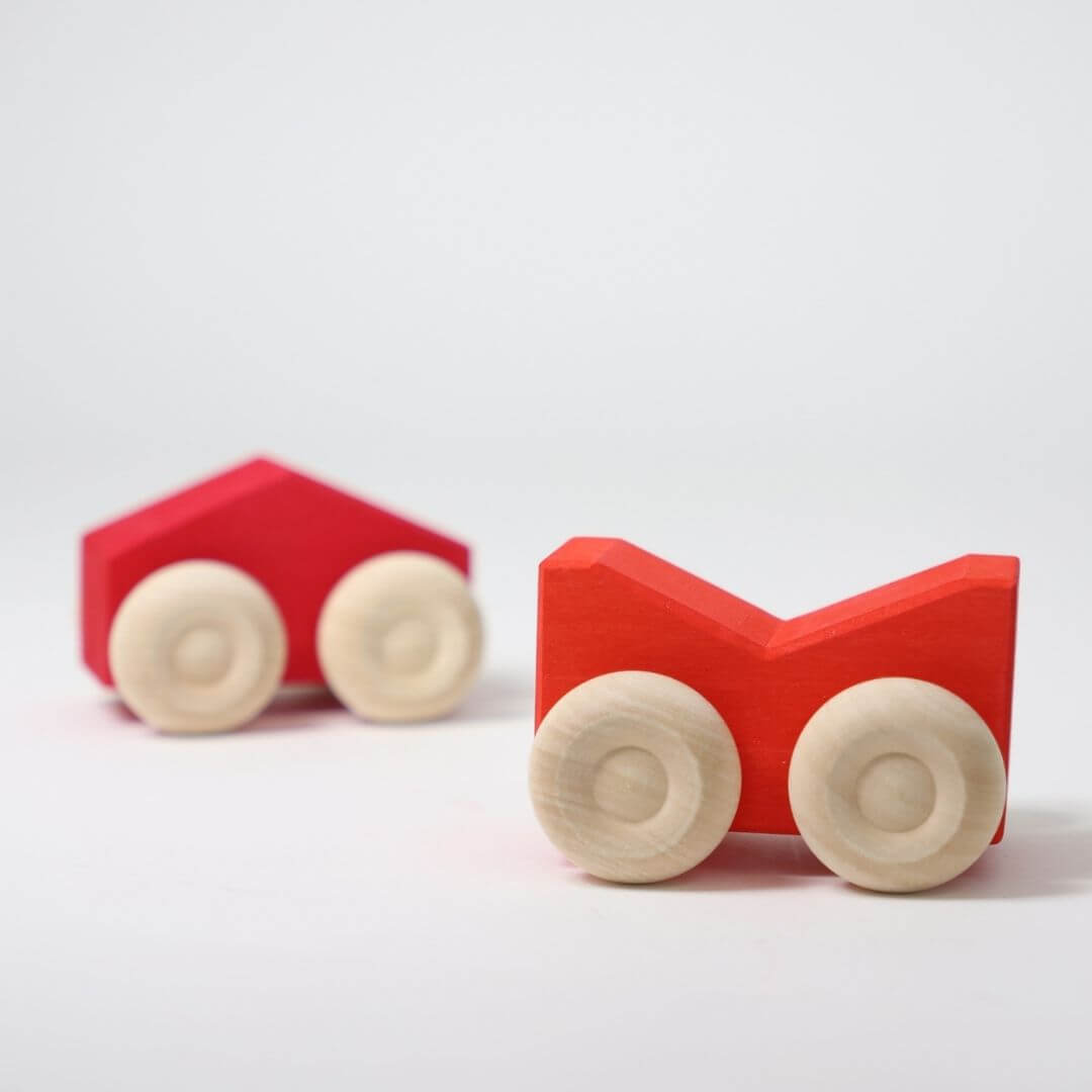 Two red wooden stacking cars by Grimm’s, handcrafted with natural wood wheels and smooth, colorful bodies for open-ended building and rolling play.