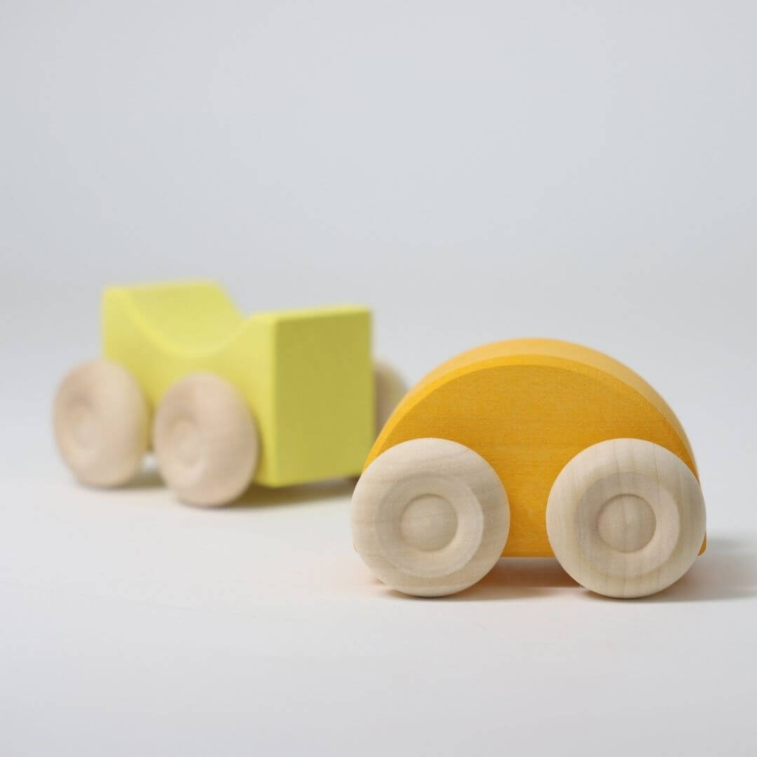 Two yellow wooden stacking cars by Grimm’s, handcrafted with natural wood wheels and smooth, colorful bodies—perfect for open-ended building and rolling play.
