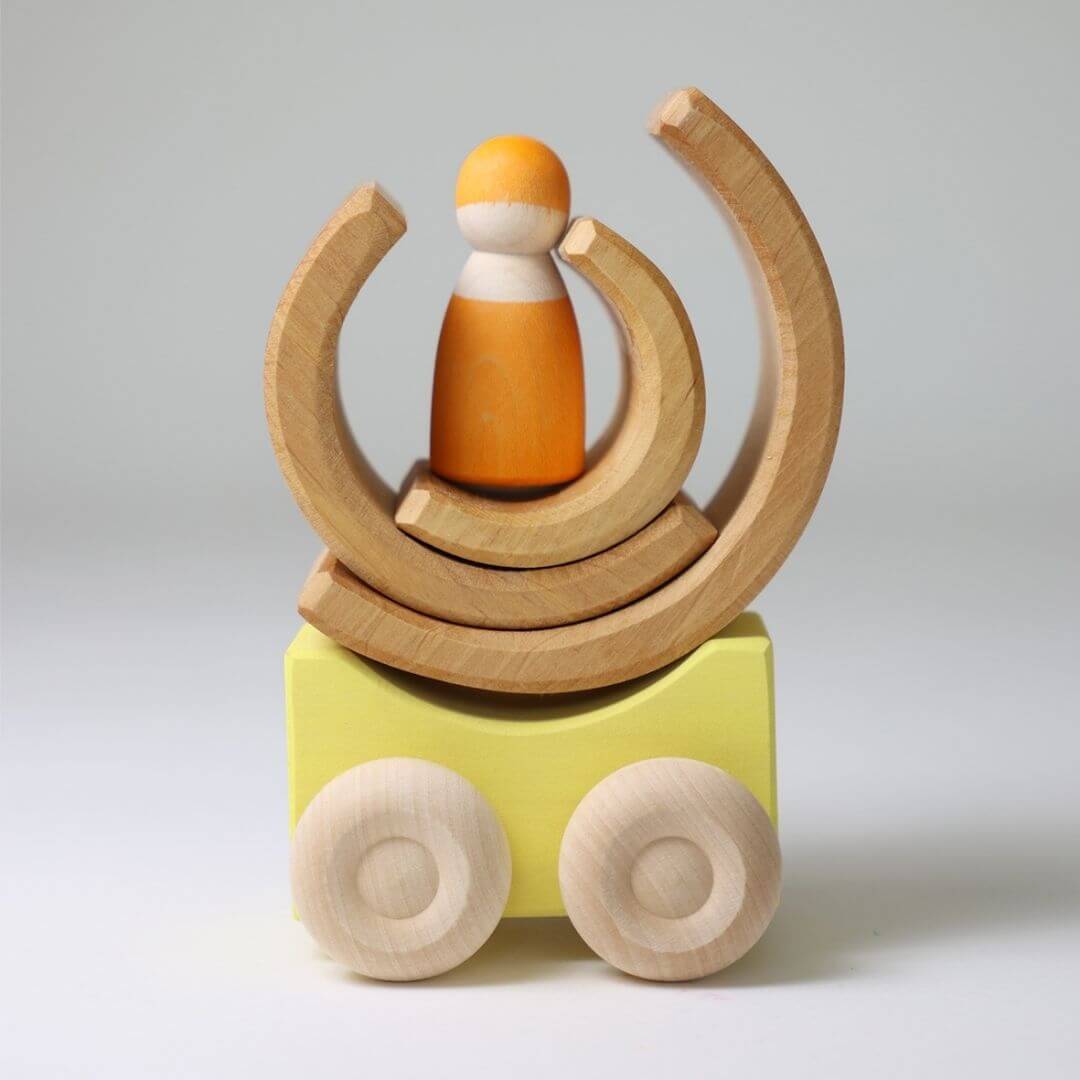 Yellow Grimm’s stacking car with natural wood wheels, topped with curved nantural wooden blocks and orange nin figure showing creative, open-ended building possibilities. Bella Luna Toys