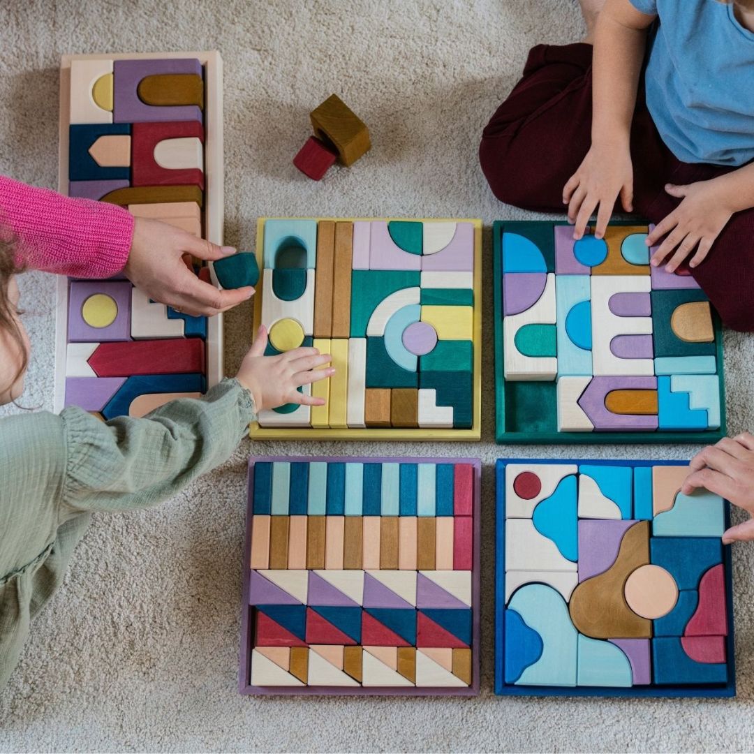 Children picking up blocks from the Grimm's Tiny Art Collection that are laid out on the floor.