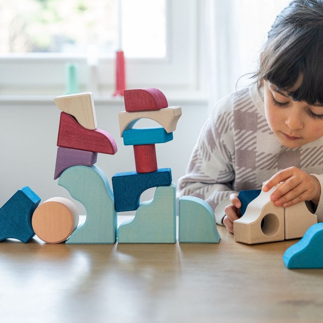 A child building with blocks from the Grimm's Wooden Toys Tiny Art Collection.