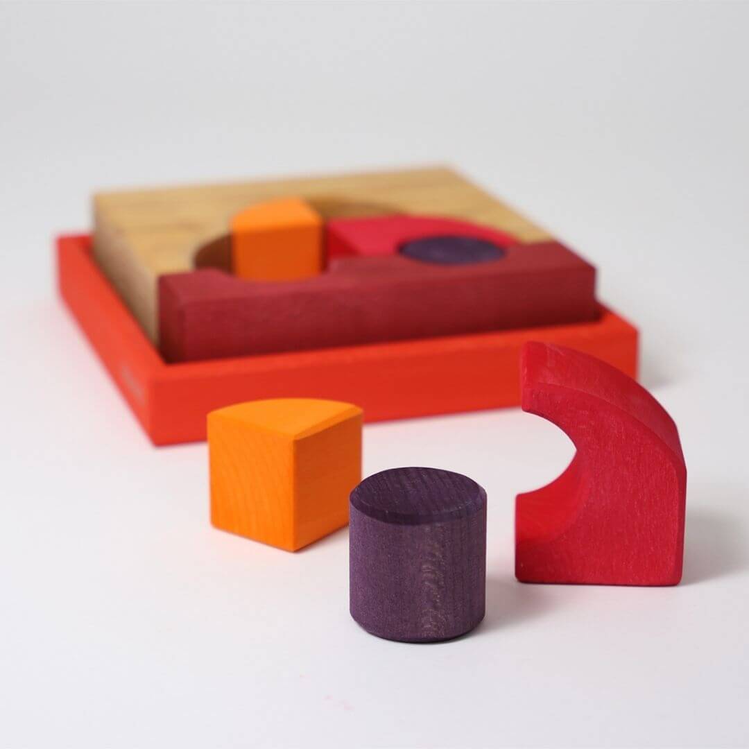 Grimm’s Wooden Puzzle and Building Set in red shown with pieces removed from the tray, including curved and circular wooden blocks for open-ended play. Bella Luna Toys