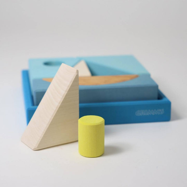 Grimm’s Wooden Puzzle and Building Set in blue shown with organic-shaped pieces arranged outside the frame, forming playful sculptures and designs. Bella Luna Toys