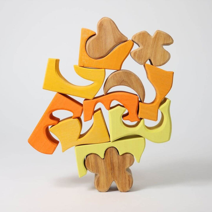 Grimm’s Wooden Puzzle and Building Set in yellow shown with organic-shaped pieces arranged outside the frame, forming playful sculptures and designs. Bella Luna Toys
