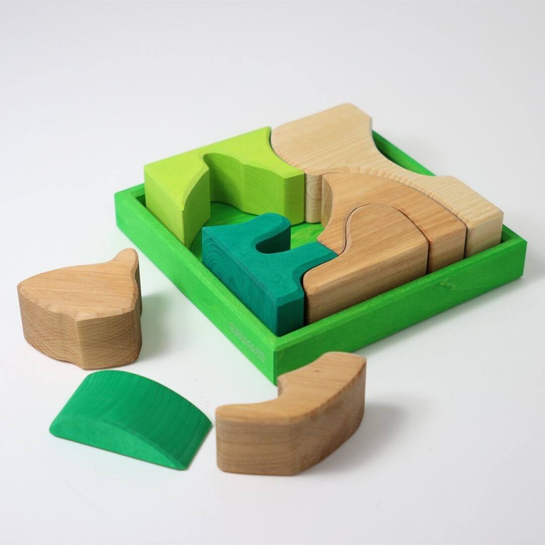 Grimm’s Wooden Puzzle and Building Set in green shown with organic-shaped pieces arranged outside the frame, forming playful sculptures and designs. Bella Luna Toys