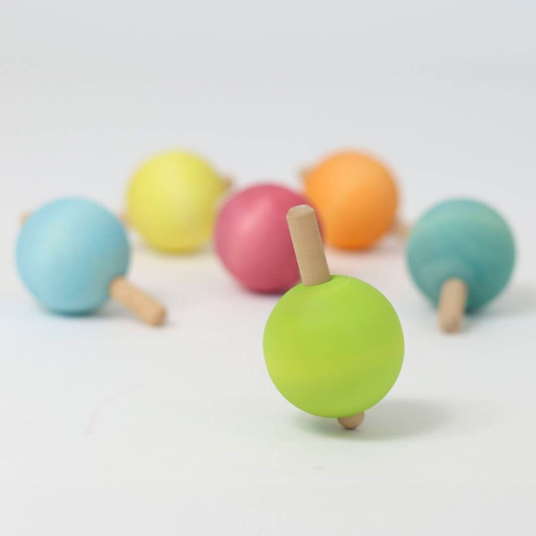 Six colorful wooden spinning tops arranged on a white background, each with a round ball handle, crafted by Grimm’s.