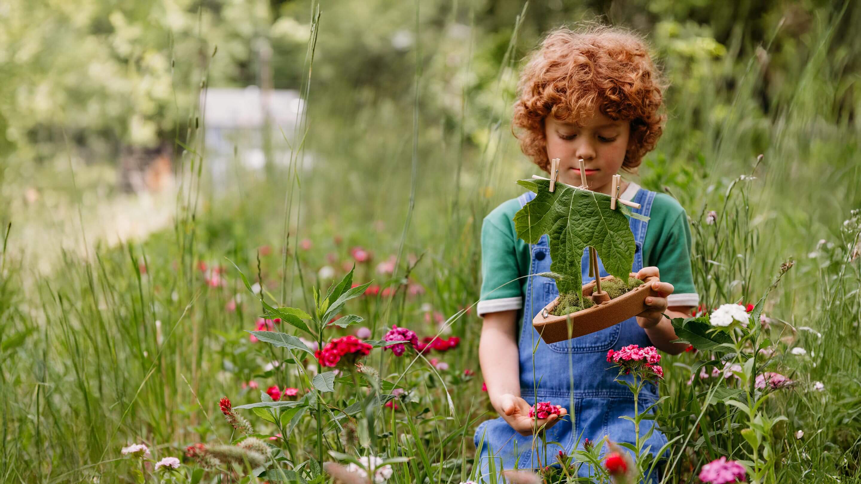 Child holding a cork boat toy with flowers and greenery.