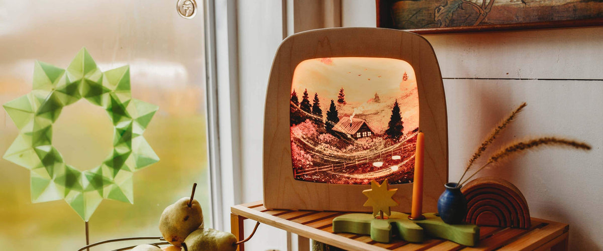 A Toverlux scene displayed on a small wooden shelf next to a window, with decorative green origami paper and rustic items around it.