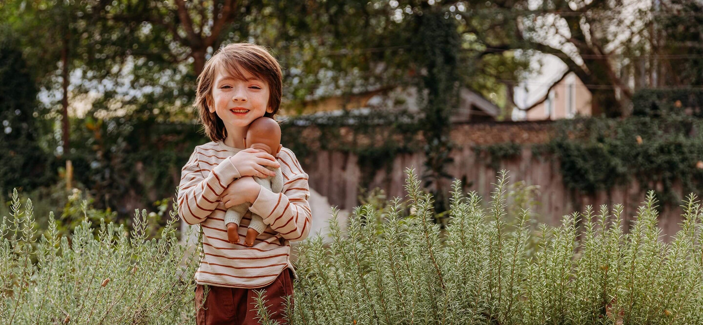 A boy is holding a Miniland baby doll in a field of grass.