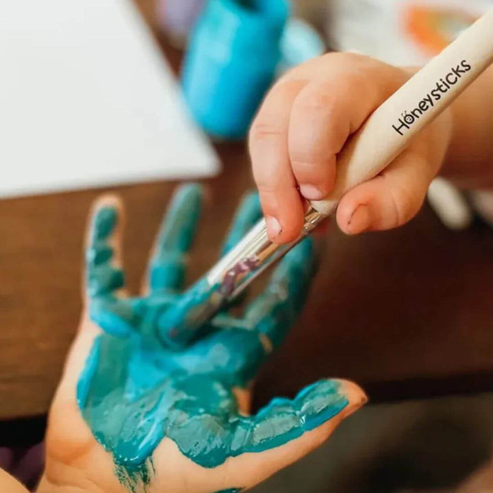 Hand with blue paint holding a Honeysticks paintbrush