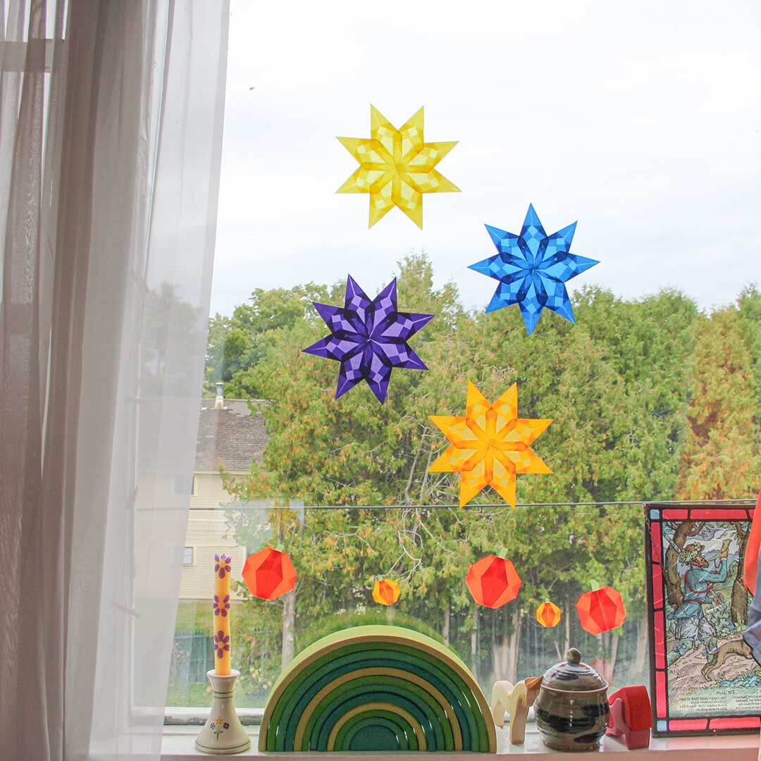 Colorful star-shaped window decorations in front of a window with a view of trees.
