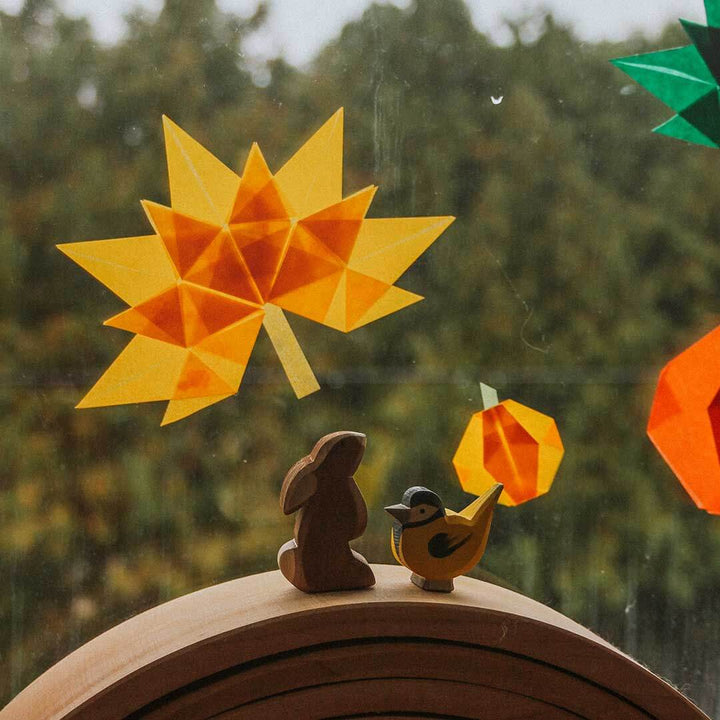 Decorative autumn scene with geometric leaf, bird, and rabbit figurines on a wooden surface.