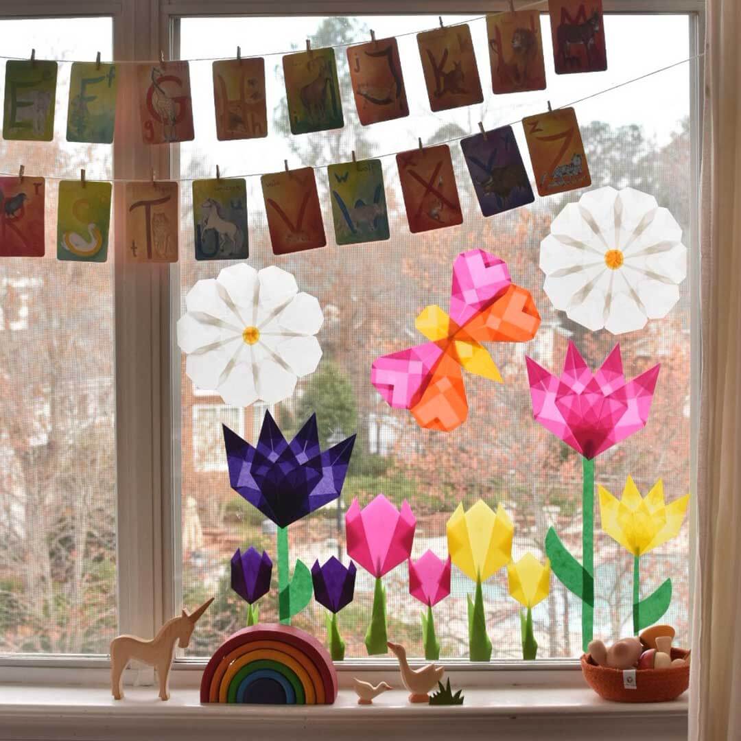 Decorative window with colorful paper flowers, letters, and small figurines.