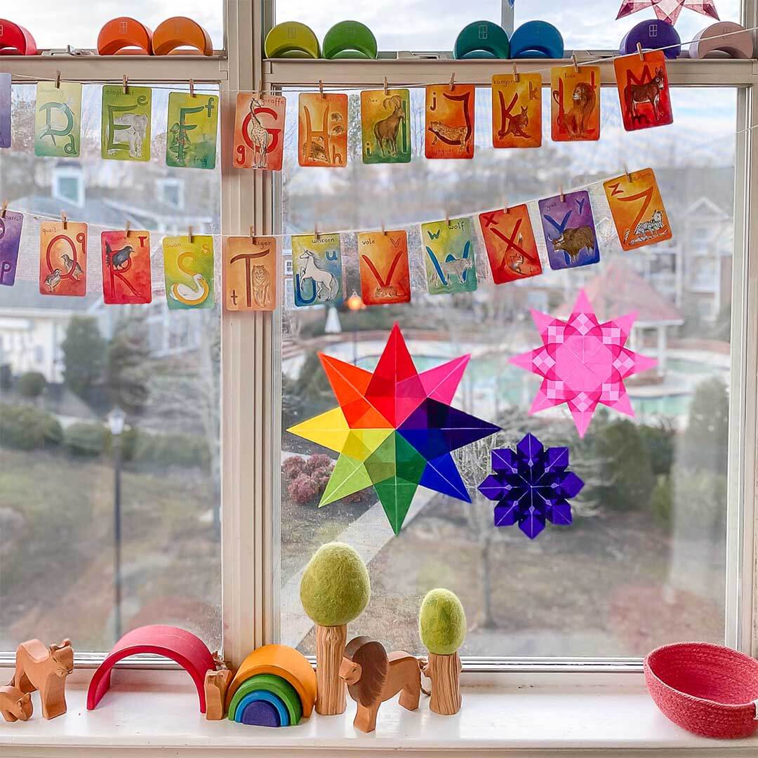 Colorful star-shaped decorations and alphabet cards hanging on a window sill with outdoor view.