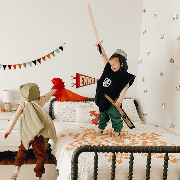 Two children playing in a bedroom with costumes and props.
