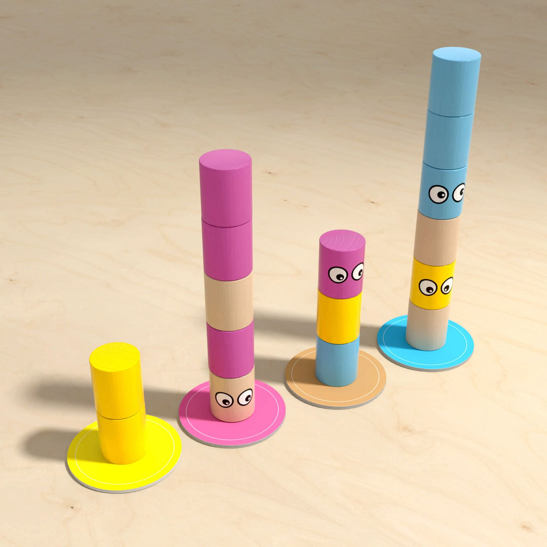 Four stacks of colorful cylindrical blocks with eyes increasing in height from left to right, on a wooden surface.