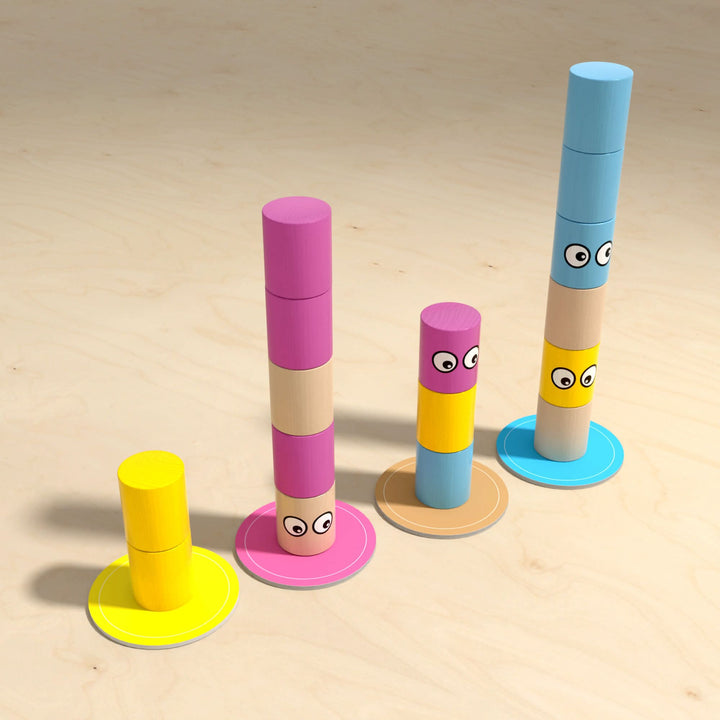 Four stacks of colorful cylindrical blocks with eyes increasing in height from left to right, on a wooden surface.