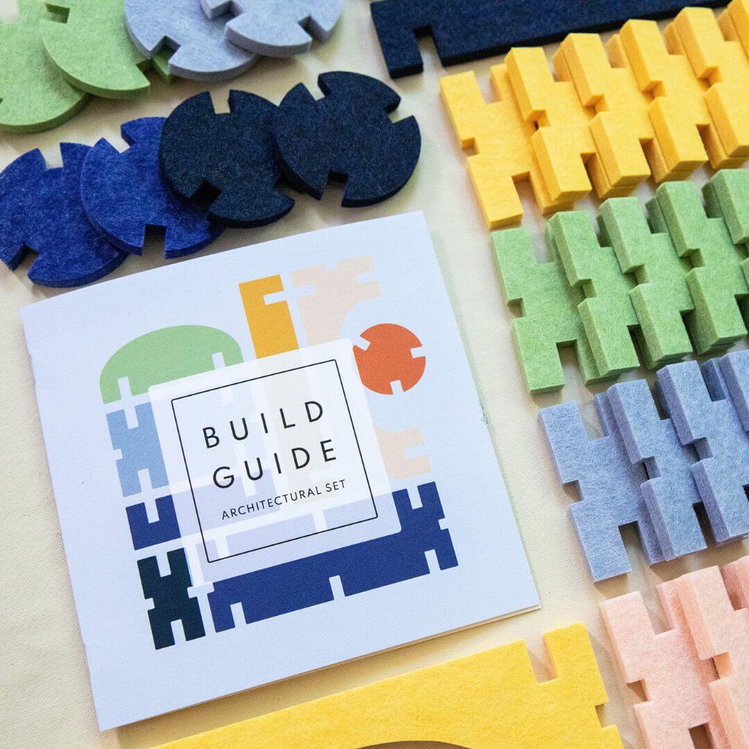 Close up image of the Lowercase Toys 92-piece Architectural Felt Block Set with colorful interlocking recycled felt pieces, including blocks, arches, domes, joiners, and build guide.