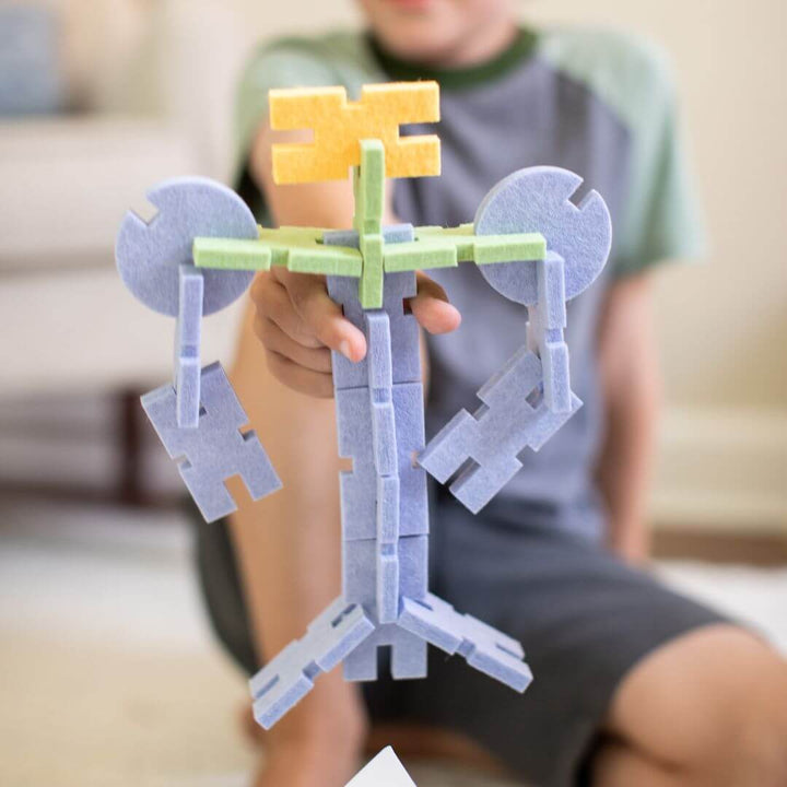 Child holding a tall robot-shaped creation made from blue, green, and yellow felt building blocks from owercase Toys.
