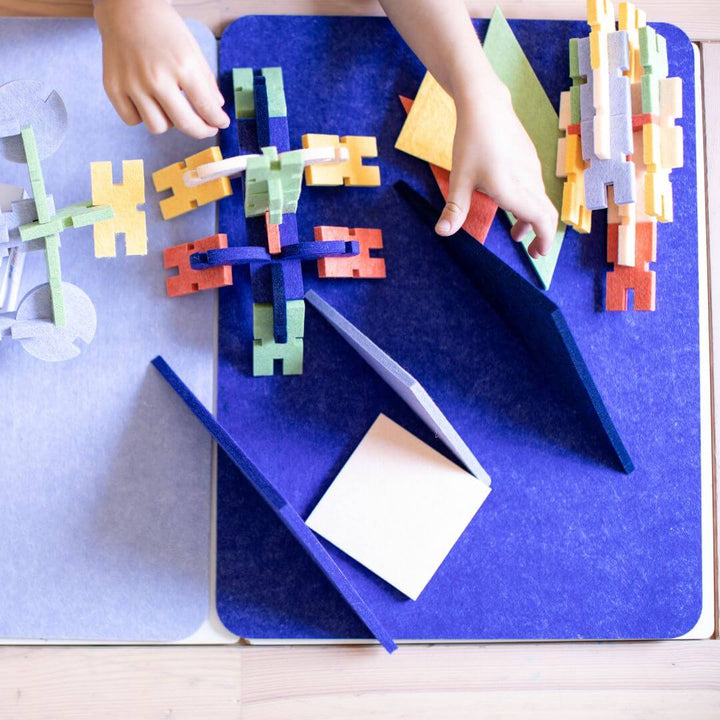 Colorful structures built with the Architectural Felt Block Set from Lowercase Toys displayed on a blue mat.