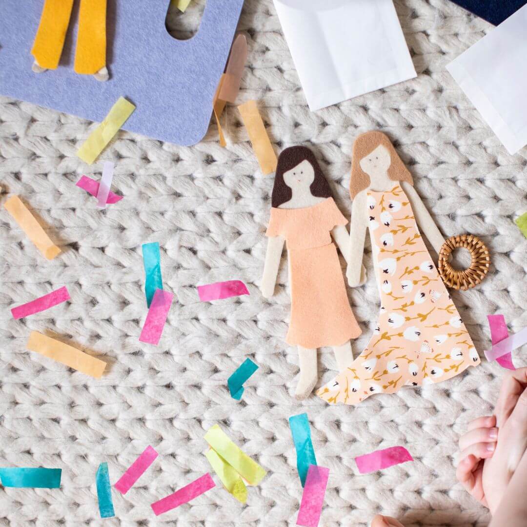 Two eco-friendly felt dolls from Lowercase Toys with mix-and-match outfits shown on a textured rug with colorful felt confetti.