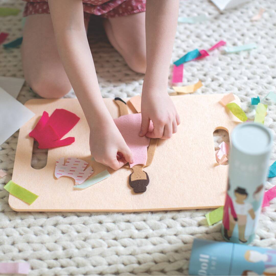 Child’s crouching down and placing felt clothing on a felt doll from Lowercase Toys with mix-and-match outfit pieces spread out on a play mat.