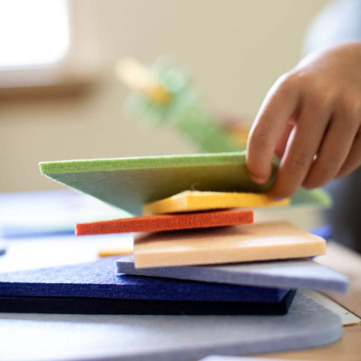 Child’s hand stacking large felt Tangram pieces from Lowercase Toys in a pile, showing the sturdy, oversized blocks.