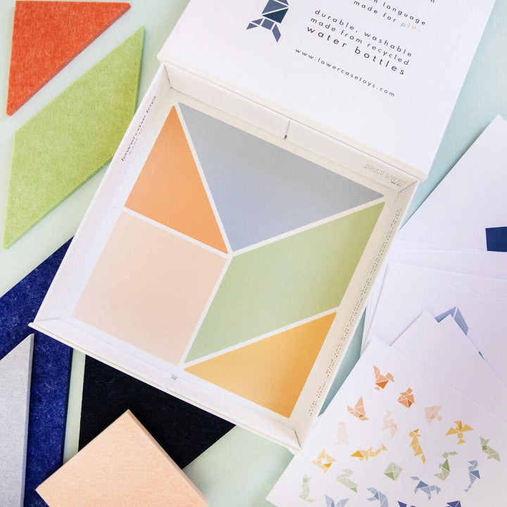 The Lowercase Toys Tangram Felt Set's open box shown with an image of 7 colorful geometric pieces arranged inside, surrounded by extra puzzle cards and felt shapes.