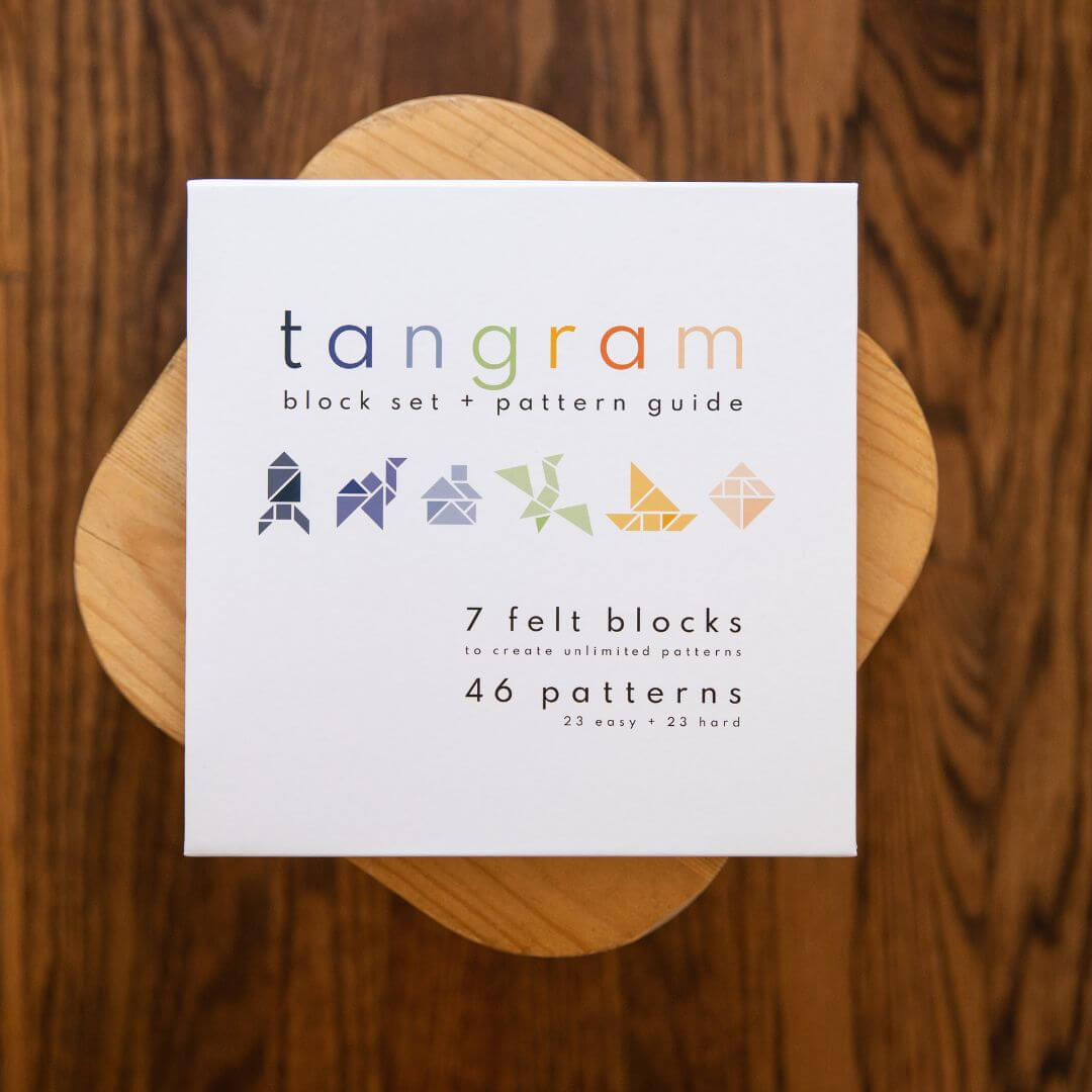 The outside ofLowercase Toy's Tangram Felt Set box on a wood stool.