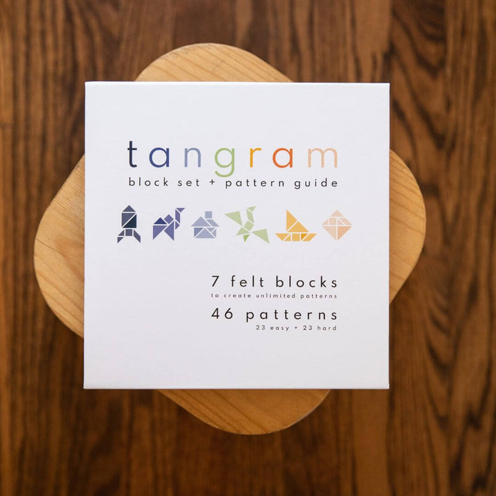 The outside ofLowercase Toy's Tangram Felt Set box on a wood stool.