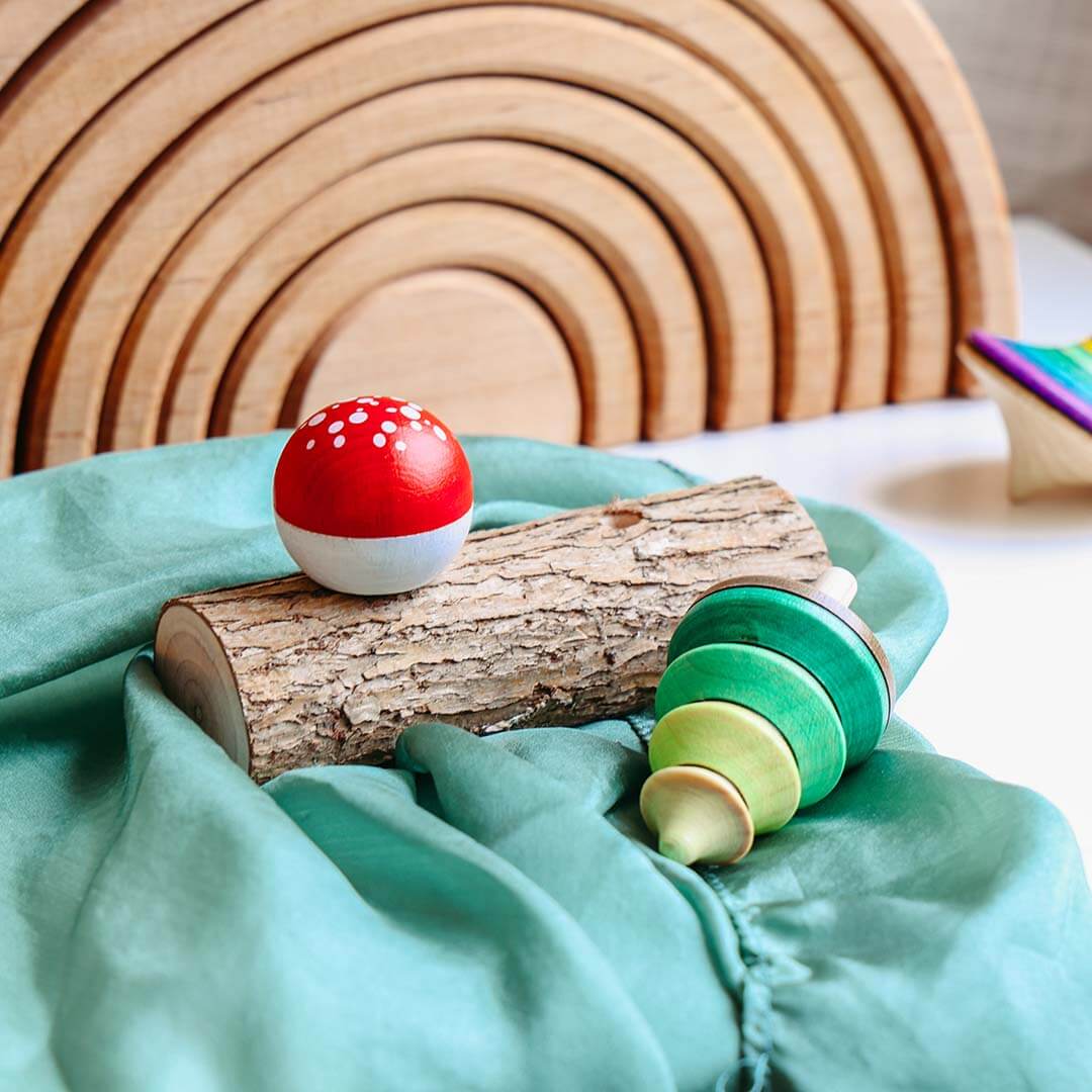 Wooden toy with a red mushroom and green cylindrical piece on a teal surface, with wooden rings in the background.