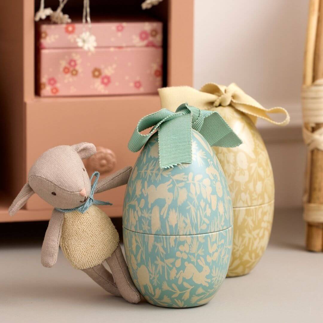Maileg stuffed lamb leaning against mint floral metal Easter egg with ribbon bow, yellow egg in background